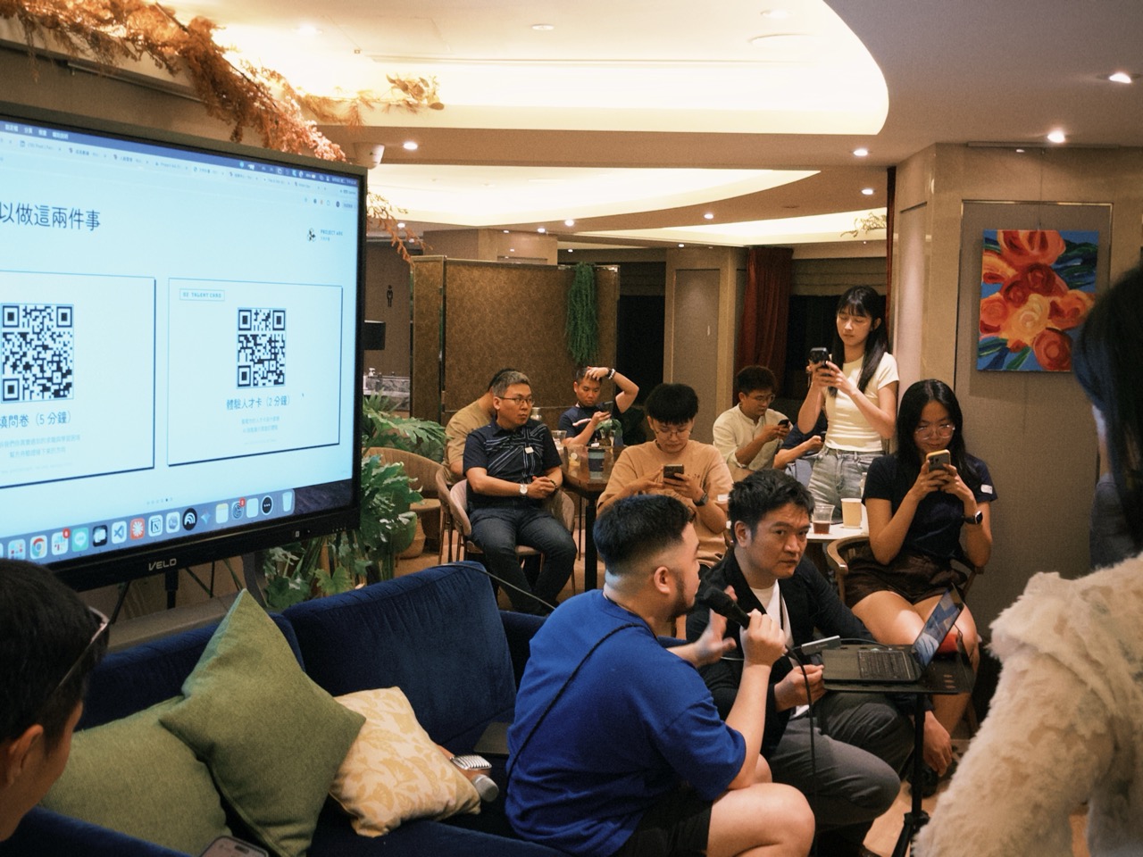 電視螢幕上顯示兩個 QR Code，後方是現場的參與者