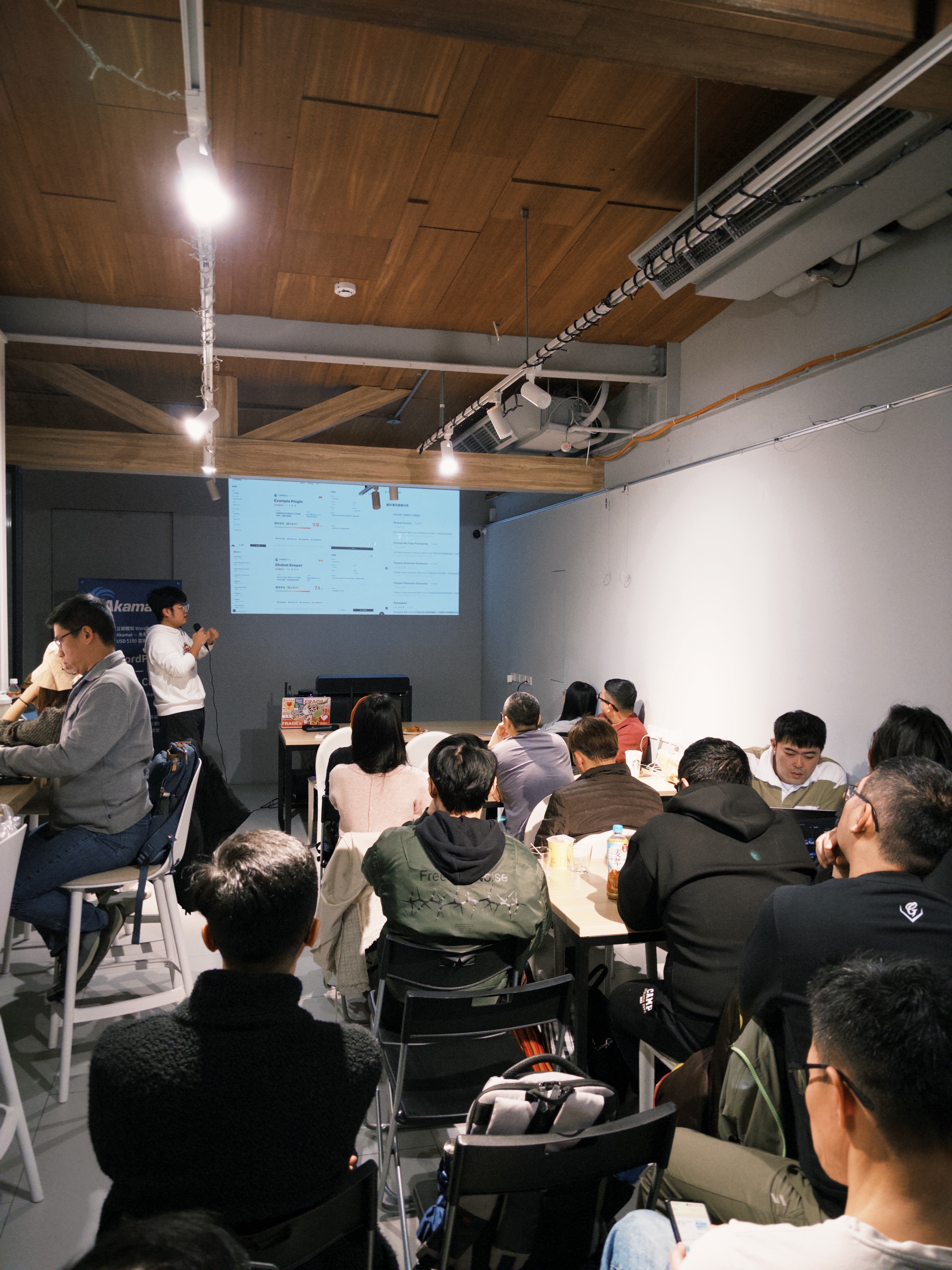 參與者坐在場地裡聆聽分享，前方投影幕播放簡報