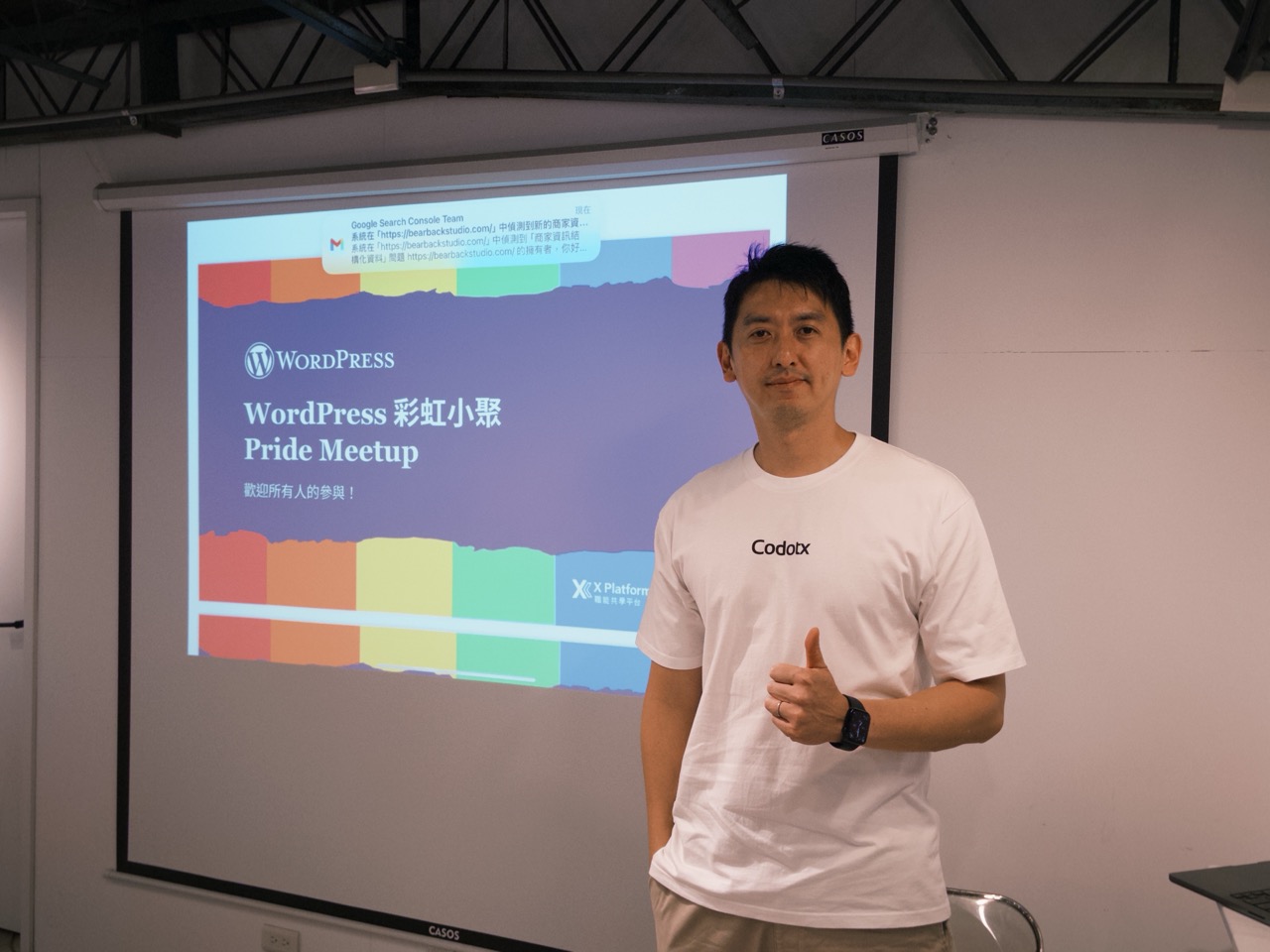 講者站在 WordPress 彩虹小聚的投影幕前比讚